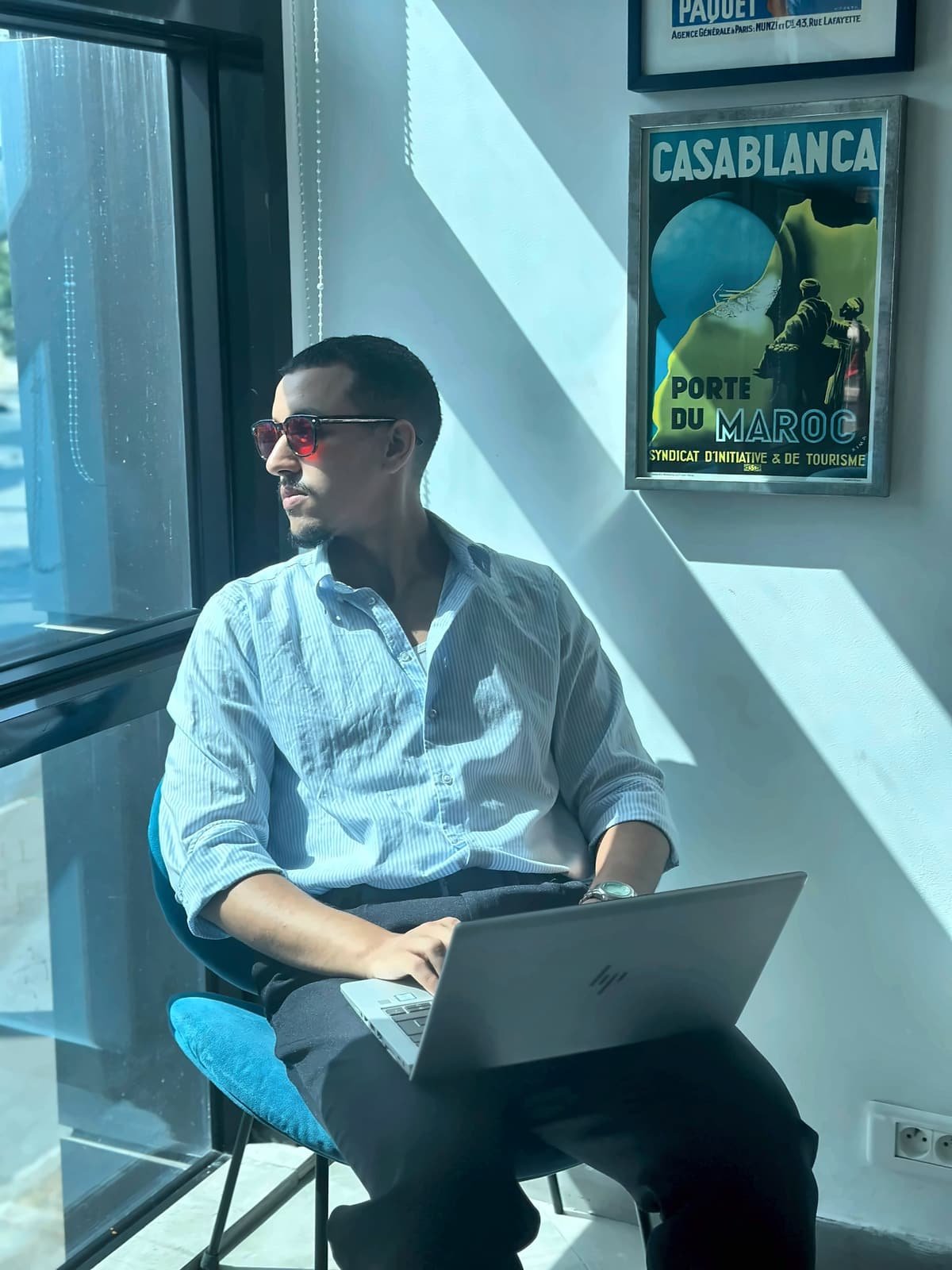 Homme portant des lunettes Bleuvex Noctis aux verres rouges, assis au soleil devant une affiche de Casablanca